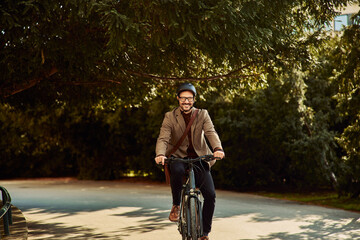 Portrait of a smiling man in a suit riding a bicycle through a park on a way to work..