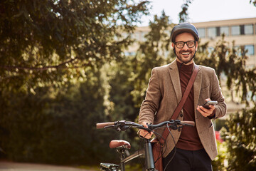 Portrait of a cheerful businessman using a mobile phone and pushing a bicycle.