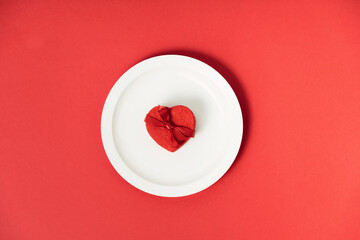 Valentine's day concept. White plate with heart shaped gift box on red background