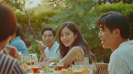 Young Asian woman visit the family during party outdoors in the garden. Attractive diverse group of people having dinner, eating foods, celebrate weekend reunion gathered together at the dining table