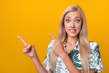 Photo of funny impressed woman with straight hair dressed shirt directing empty space biting lips isolated on yellow color background