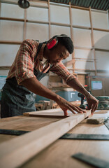 African male lines up piece of wood while working on carpentry project in woodwork warehouse 