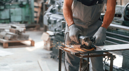 Polishing the surface with angle grinder. Close up view of man that is working at the factory