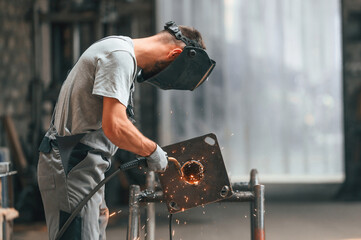 Process of welding. Young factory worker in grey uniform