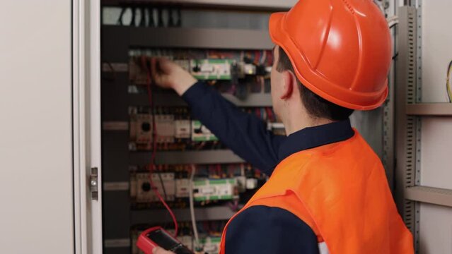 Multimeter testing, Factory maintenance, Voltage testing. Electrician carries out measurements using multimeter to assess current in control panel at factory.
