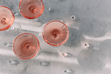 Glasses with cold pink champagne placed on table near cubes of ice