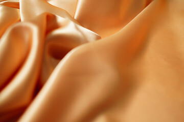 Close-up of yellow silk satin, draped fabric, gold color, elegant background. Beautiful wavy area...