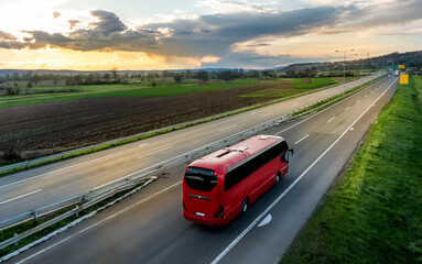 Red Modern comfortable tourist bus driving through highway at bright sunny sunset. Travel and coach tourism concept. Trip and journey by vehicle - obrazy, fototapety, plakaty