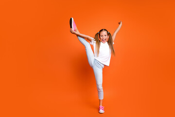 Full length portrait of overjoyed sporty girl hand hold stretch leg empty space isolated on orange color background