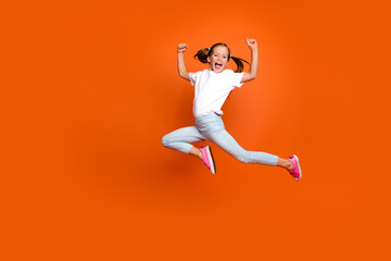 Full length portrait of overjoyed delighted girl jump raise fists success empty space isolated on orange color background