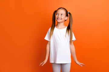 Photo portrait of charming little girl look interested empty space cute pose wear trendy white clothes isolated on orange color background