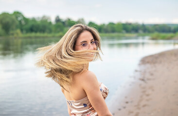 glückliche junge Frau mit wehenden Haaren steht am Fluss