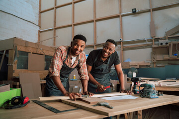 Young male African American colleagues measure piece of wood while working on carpentry project 