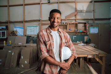 Smiling African male with hardhat under arm poses for picture in woodwork factory 