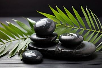 Black spa stones with palm leaves on wooden background