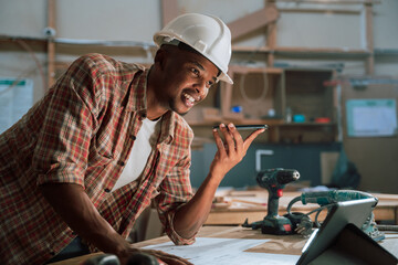 Medium shot of African male talking on the phone in a carpentry factory  - obrazy, fototapety, plakaty