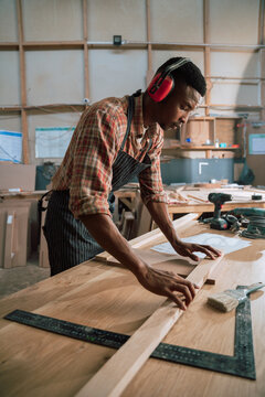 Young African American male in carpentry factory wears earmuffs while working 
