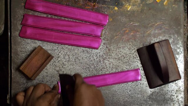Craftsman making handmade lac bangles popular in India - Small scale industry . Indian worker cutting flattened pink-colored lac bangles into the perfect shape from the corners using a tool