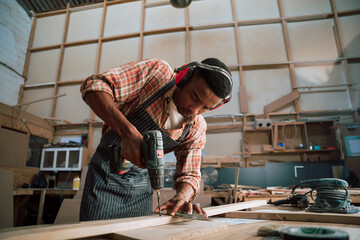 African American carpenter drills a piece of wood in carpentry workshop 