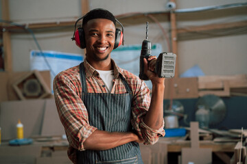 Smiling African American male poses with electrical drill in woodwork workshop 