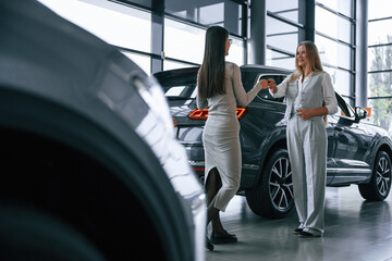Giving the keys. Female manager is helping woman customer in the car dealership salon
