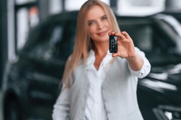 Fototapeta premium Holding keys. Woman in formal clothes is in the car dealership