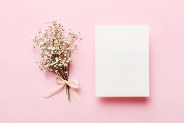 Fotobehang Wedding mockup with white paper list and flowers gypsophila on colored table top view flat lay. Blank greeting cards and envelopes. Beautiful floral pattern. Flat lay style © sosiukin