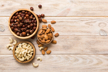 Assortment of nuts in wooden bowl on colored table. Cashew, hazelnuts, walnuts, almonds. Mix of nuts Top view with copy space