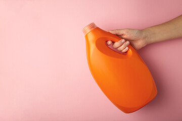 Hand with liquid laundry detergent bottle, cleaning soap for cloth on pink background. Space for...