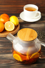 Glass teapot with cup and citrus on brown background.