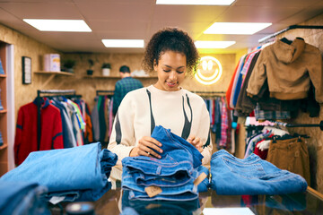 Female Sales Assistant Or Customer Sorting And Looking At Stock Of Jeans In Fashion Or Clothes Store