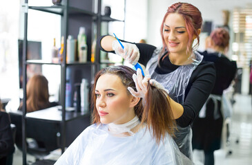 Professional female hairdresser applying color to female customer at design hair salon, woman having her hair dyed