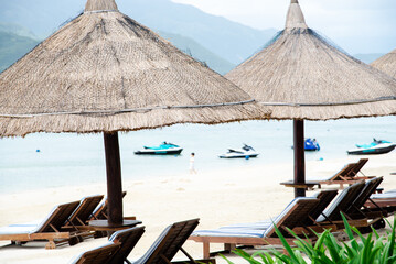 Beach umbrella thatched with palm leaves, lounge chairs, white sandy shoreline and row of personal...