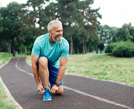 Portrait of a happy active mature or middle aged  senior man posing fixing shoelace on his running shoe after exercising outdoors, vitality and active senior concept - Powered by Adobe