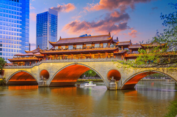 Traditional Chinese Bridge at Twilight with Illuminated Arches, Modern Skyline, and Boat in East Asia - obrazy, fototapety, plakaty