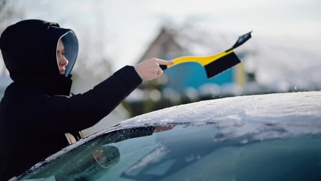 Woman Cleaning Car from Snow in Winter. Driver Brushing Snow off Car with a Brusher Scraper