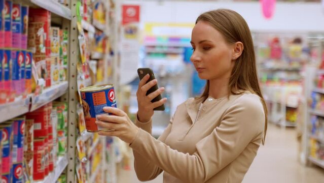 Satisfied woman chooses food for her puppy in a pet store by scanning a QR code with her smartphone. 