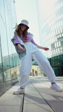 Fashionable funky caucasian girl dancer in sportswear is performing outdoor street dancing motion . slow motion video. Joyful summer female artist demonstrate choreography in the city.