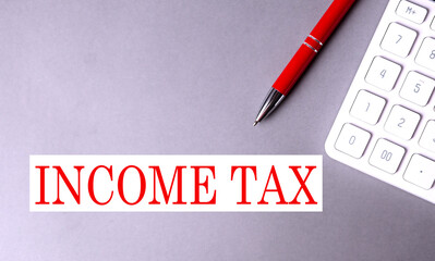 INCOME TAX text written on a gray background with pen and calculator