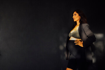 Fashionable attractive pregnant woman posing in dark clothes in the studio