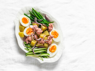 Breakfast, appetizers, snack plate - boiled eggs, potatoes, string beans, red onion, cucumber, canned tuna salad on a light background, top view