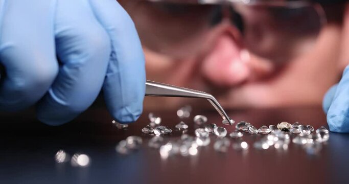 Jeweler evaluating gems with tweezers in workshop closeup 4k movie slow motion. Diamond quality assessment concept
