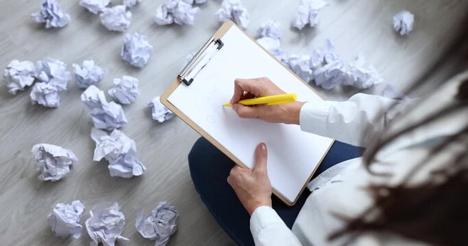 Woman sitting on floor near crumpled and scattered papers and writing business plan closeup 4k movie slow motion. Difficulty working in business concept