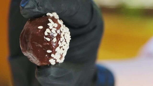 Chef scatters sesame seeds on ball-shaped candy. Master class conducted by skilled confectioner utilizing readily available ingredients
