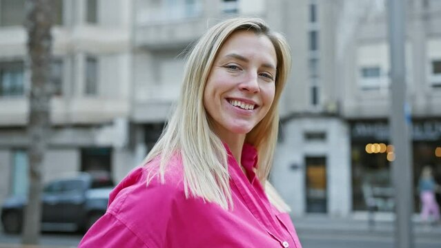 Caucasian woman with blonde hair wearing a pink shirt smiles on a city street, evoking urban lifestyle and leisure.