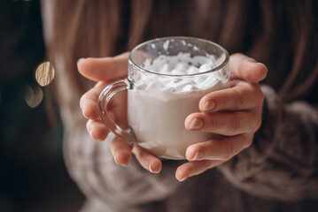 Transparent glass mug of cocoa with marshmallows in female hands. Close-up. New Year's portrait.