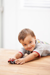 Naklejka premium Cars, toys and portrait of child by table playing for learning, development and fun at modern home. Cute, sweet and boy kid enjoying a game with plastic vehicles by wood for childhood hobby at house.
