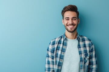 Portrait of a handsome man with a friendly smile, wearing a smart casual outfit, standing against a plain blue background. - obrazy, fototapety, plakaty