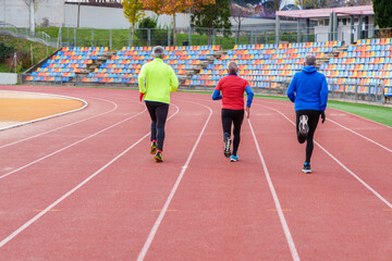Group of elderly friends enjoying a jog together on a red running track, showcasing teamwork and...