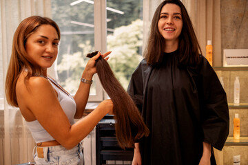 Pretty brunette young woman looks into a huge mirror when her luxurious long hair is cut off